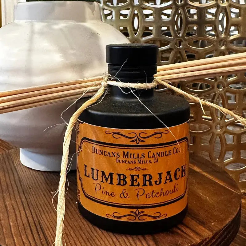 A bottle of Lumberjack Reed Diffuser with natural reeds, evoking the rugged scent of sugared pine and patchouli, inspired by the forests of Cazadero.