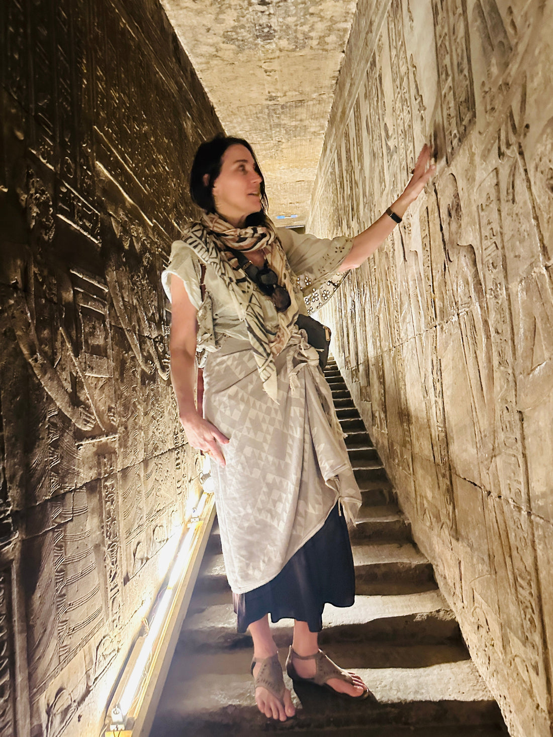 Stephanie standing in a temple corridor in Egypt, hand resting on a wall covered in hieroglyphs.