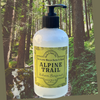 A bottle of Alpine Trail Bath Gel, infused with botanical extracts and scented with balsam and bergamot, housed in a clear recyclable PET plastic bottle and a forest background.