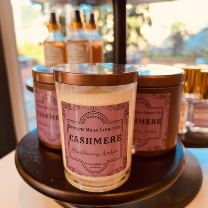Display of three lidded candles of two styles with a purple label: Cashmere, Blackberry Amber