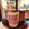 Display of three lidded candles of two styles with a purple label: Cashmere, Blackberry Amber