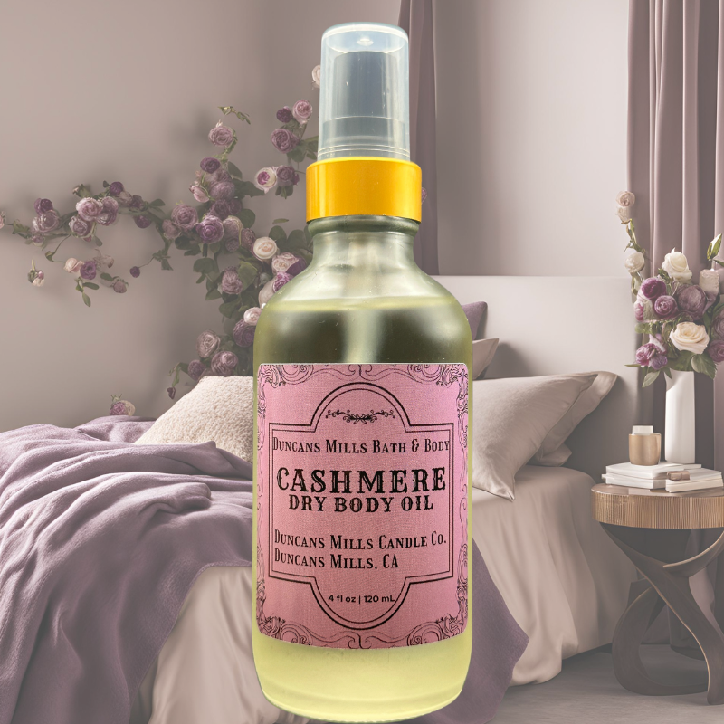 Cashmere Body Oil is displayed with a bedroom background of flowers and cozy plum blankets. 