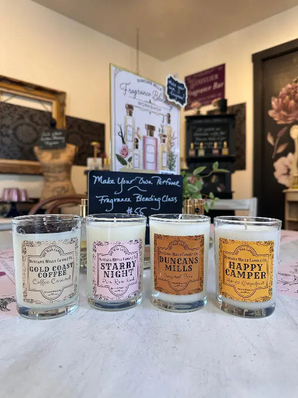 Four café glass candles: Duncans Mills, Starry Night, Gold Coast Coffee, and Happy Camper, styled in the candle shop's fragrance bar.