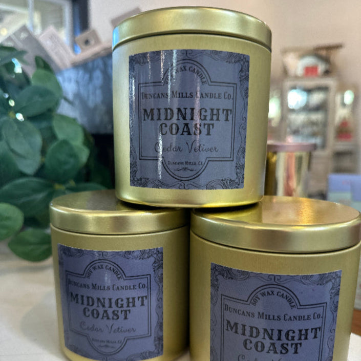 Large gold-colored candle tins with lids and deep-blue label: Midnight Coast, Cedar Vetiver