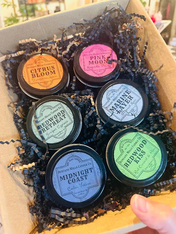 Set of black petite tin candles with labeled lids in a box with crinkle tissue.