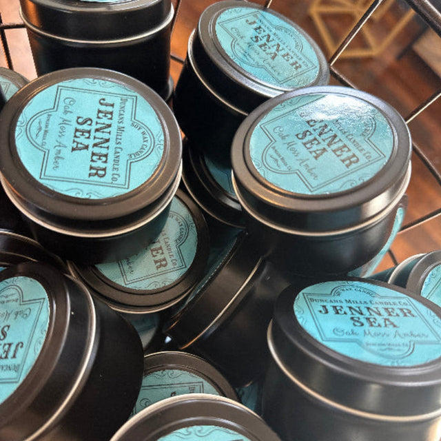 Small black candle tins with lids and light-blue label: Jenner Sea, Oak Moss Amber
