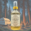 A luxurious glass bottle of Starry Night Body Oil, infused with botanical extracts on a background with towering redwoods under the night starry sky where a family is gathered around a campfire and the camper is nestled nearby.