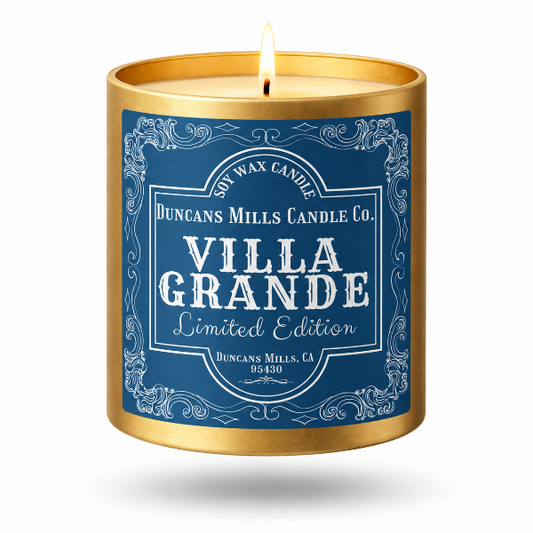 A lit soy wax candle in a cylindrical gold metal tin with a blue label reading 'Duncans Mills Candle Co. Villa Grande Limited Edition' on a white background.