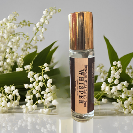 Whisper Rollerball Perfume displayed with flowers evoking its delicate and enchanting fragrance.