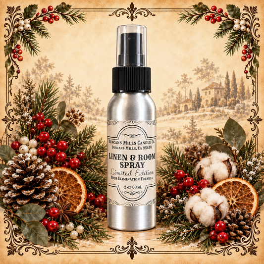 A silver spray bottle labeled 'Linen & Room Spray' by Duncans Mills Candle Co., centered against a vintage-style illustrated background and surrounded by holiday greenery, pinecones, cotton bolls, dried orange slices, and red berries.